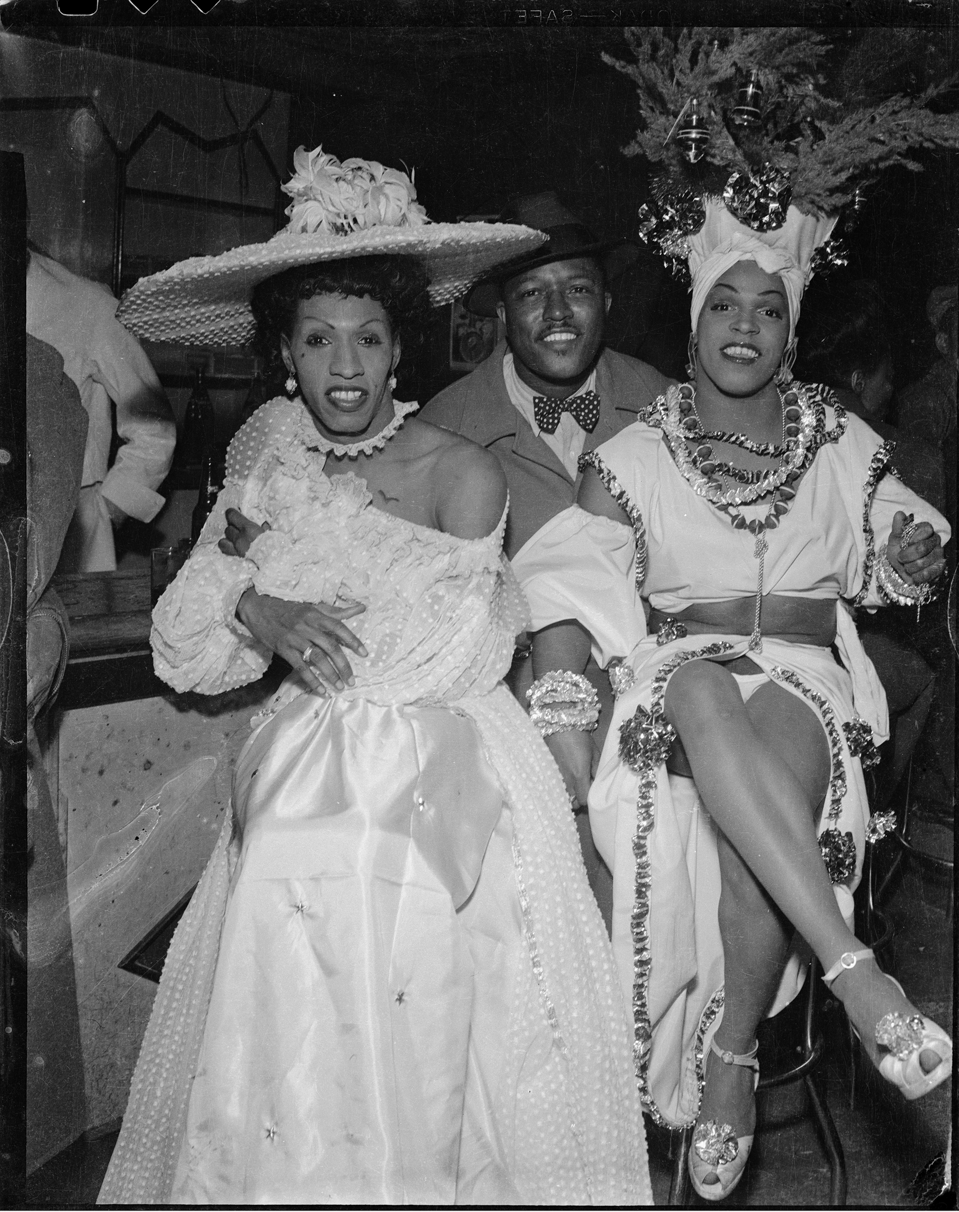     Charles “Teenie” Harris, Man seated between drag performers &#8220;Gilda,&#8221; and &#8220;Junie&#8221; Turner wearing Caribbean-style costume, 1945 – 1955.
Silver Gelatin print. Courtesy of Carnegie Museum of Art, Pittsburgh.

